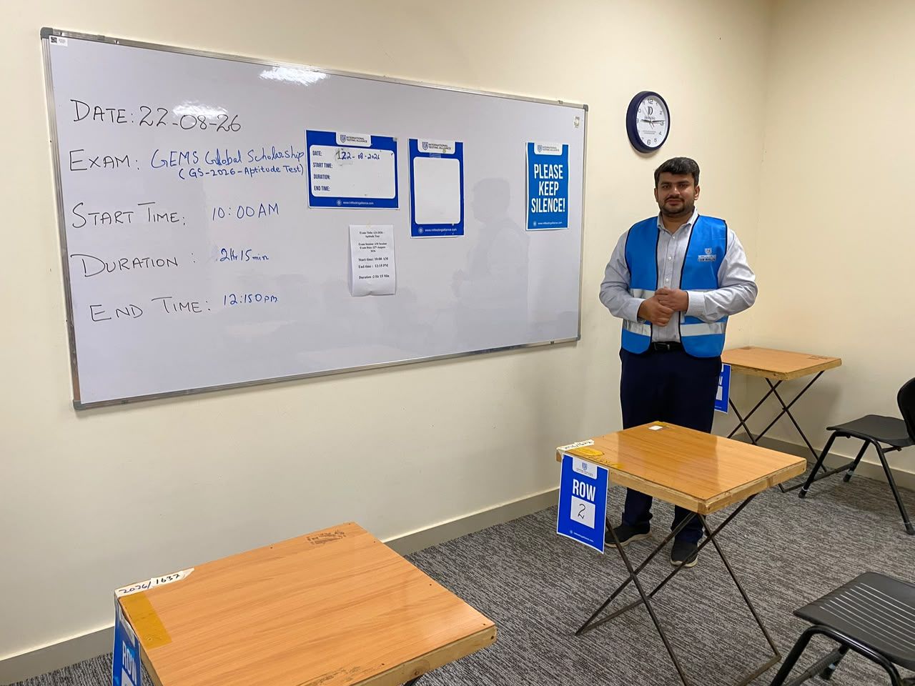 Invigilator briefing beside a whiteboard with the exam schedule